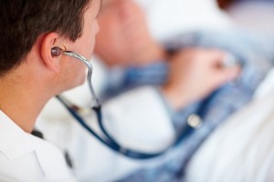 Young doctor checking an elderly man's heart beat with a stethoscope