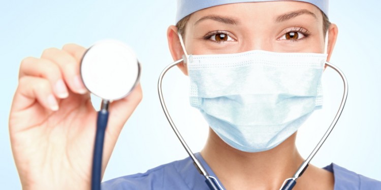 Young doctor / surgeon showing stethoscope wearing surgeon mask looking at camera. Asian / Caucasian female model.