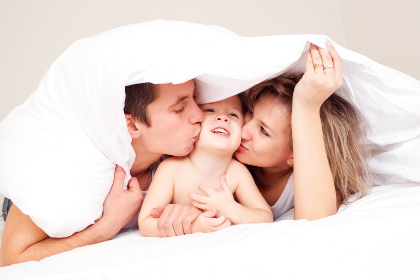 happy family, mother , father and their baby under the blanket on the bed at home